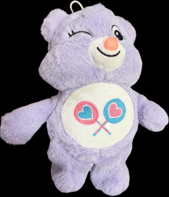 Oso de peluche lavanda Sweet Wink con lazos, ideal como regalo suave y lindo, en un entorno que muestra el osito y detalles decorativos